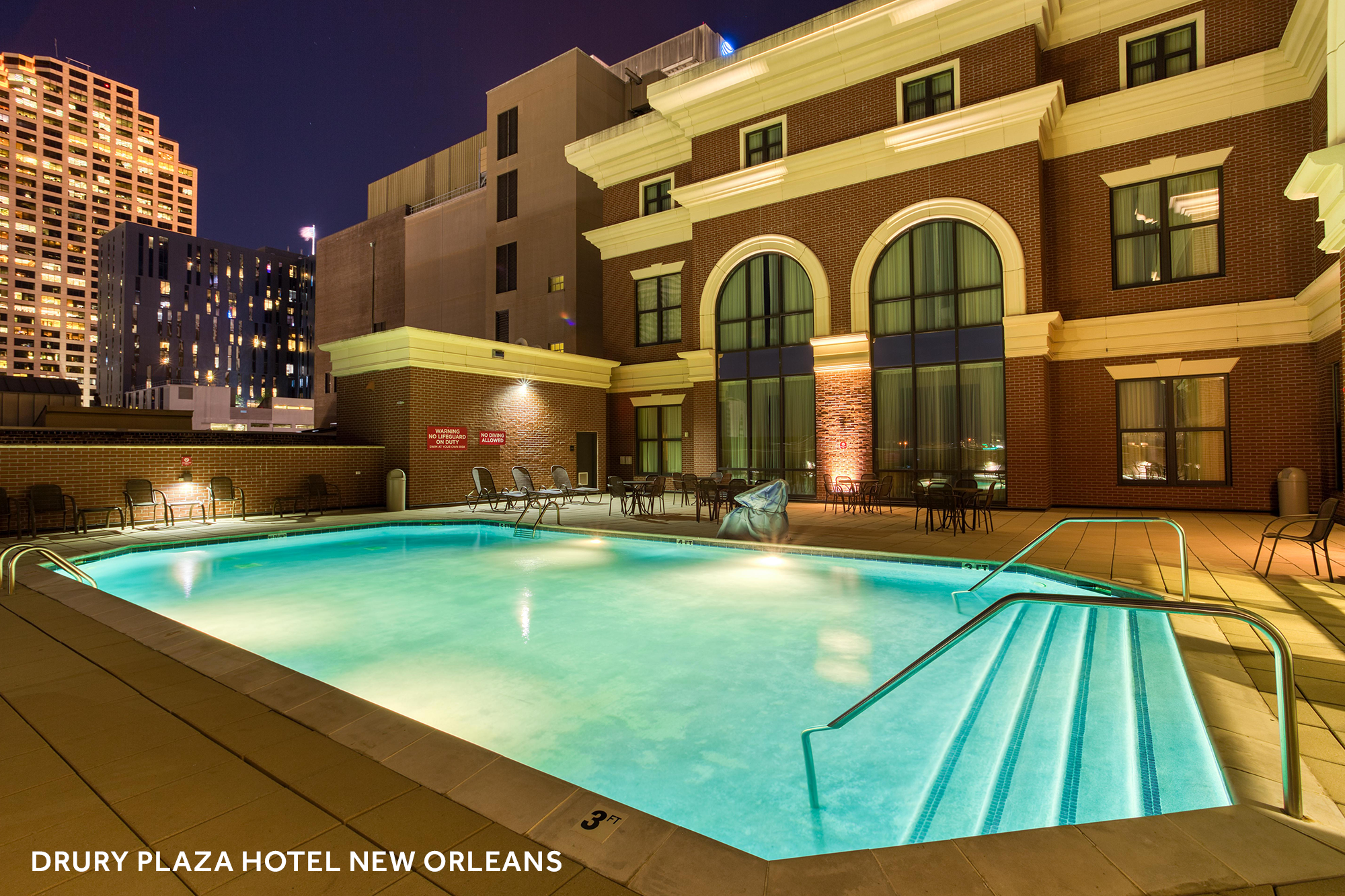 A lit up pool and seating area at night with New Orleans buildings in the background.